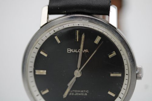 fig 5. A vintage Bulova automatic wristwatch featuring a black dial with silver baton hour markers and a black leather strap with white stitching.
