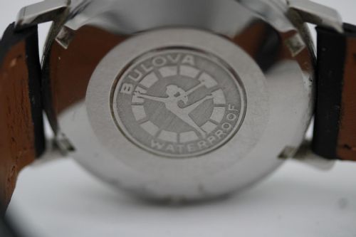 fig 7. A vintage Bulova automatic wristwatch featuring a black dial with silver baton hour markers and a black leather strap with white stitching.