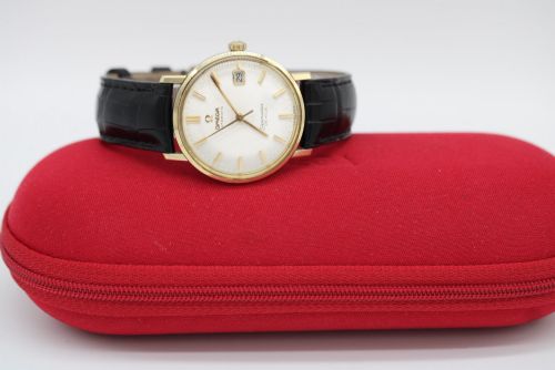 fig 1. A vintage gold-plated Omega Seamaster DeVille automatic wristwatch with a white textured dial, gold baton indices, date window, and black leather strap.