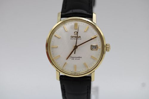 fig 3. A vintage gold-plated Omega Seamaster DeVille automatic wristwatch with a white textured dial, gold baton indices, date window, and black leather strap.