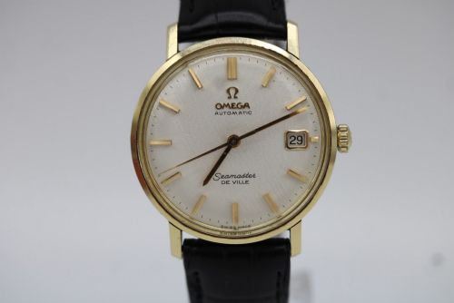 fig 6. A vintage gold-plated Omega Seamaster DeVille automatic wristwatch with a white textured dial, gold baton indices, date window, and black leather strap.