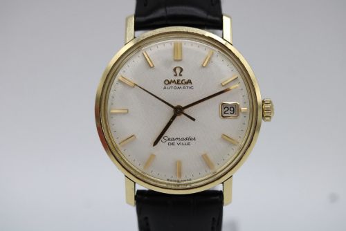 fig 7. A vintage gold-plated Omega Seamaster DeVille automatic wristwatch with a white textured dial, gold baton indices, date window, and black leather strap.