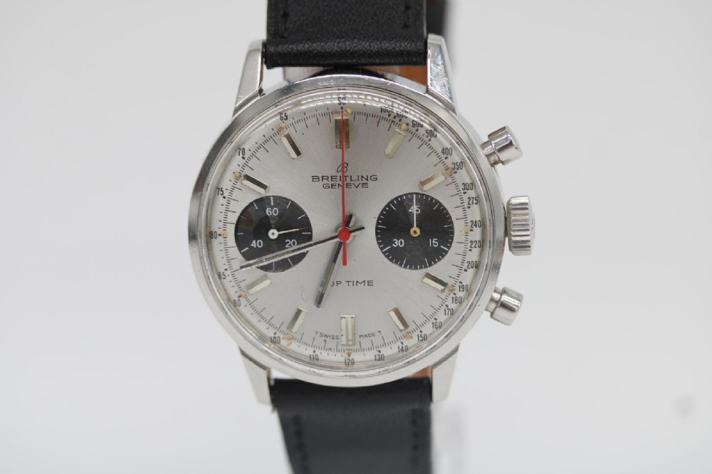 A vintage 1969 Breitling Top Time wristwatch with a silver panda dial, two black sub-dials, a central red hand, and a black leather strap.