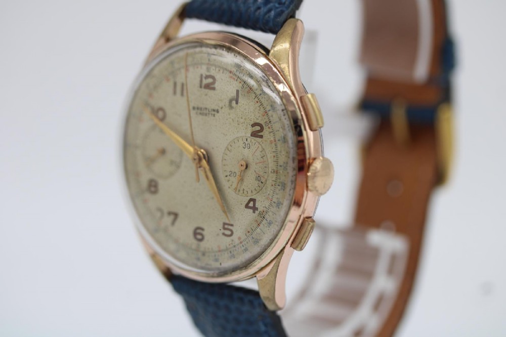 A 1950s Breitling Cadette chronograph wristwatch featuring a circular gold-plated case, twin sub-dials, Arabic numerals, and a blue textured leather strap. View II