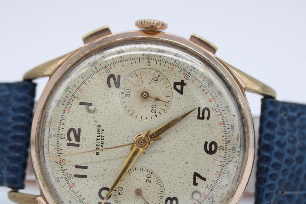 A 1950s Breitling Cadette chronograph wristwatch featuring a circular gold-plated case, twin sub-dials, Arabic numerals, and a blue textured leather strap. View IV