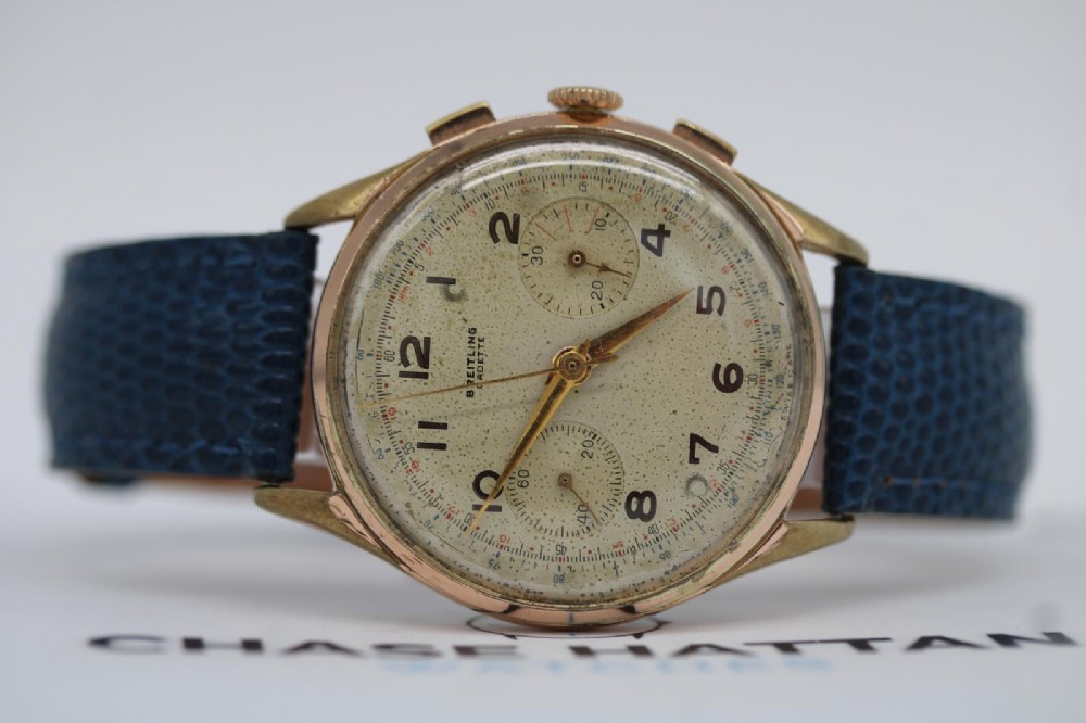 A 1950s Breitling Cadette chronograph wristwatch featuring a circular gold-plated case, twin sub-dials, Arabic numerals, and a blue textured leather strap. View V