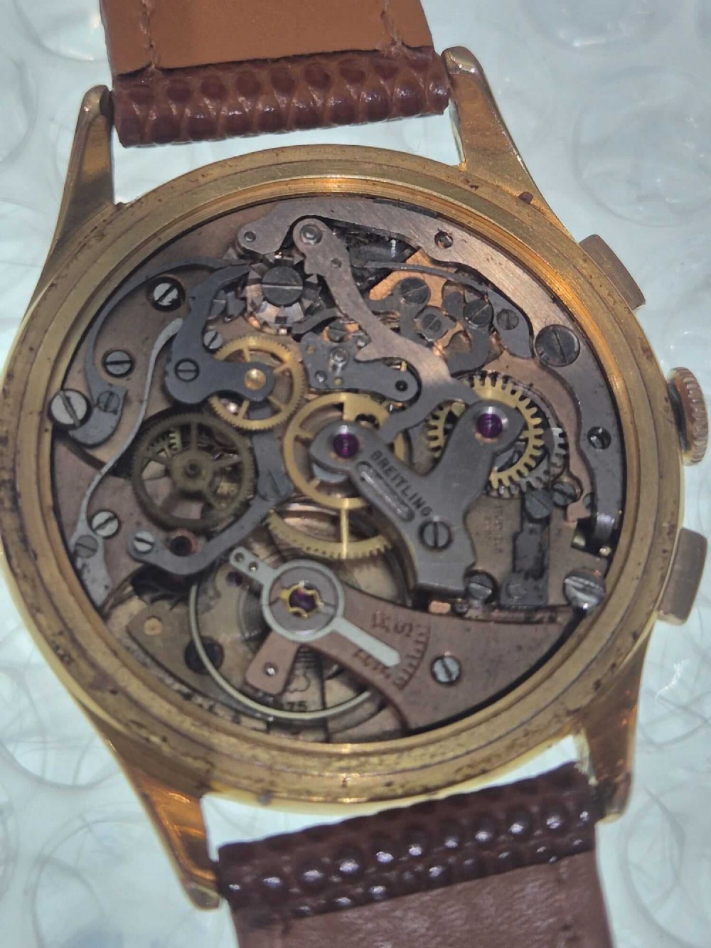 A 1950s Breitling Cadette chronograph wristwatch featuring a circular gold-plated case, twin sub-dials, Arabic numerals, and a blue textured leather strap. View X