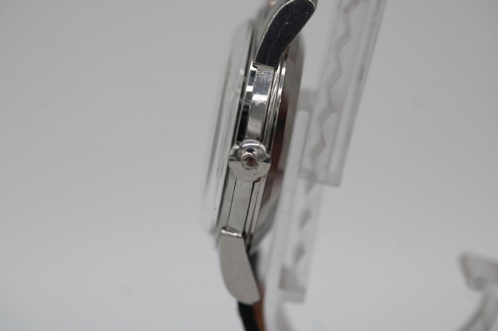 A vintage 1956 Omega Seamaster automatic wristwatch featuring a silver-coloured stainless steel case, off-white dial with gold-tone markers, and a navy blue leather strap. View VI