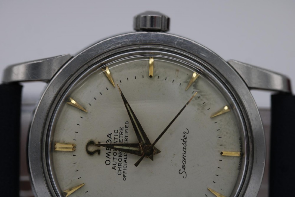 A vintage 1956 Omega Seamaster automatic wristwatch featuring a silver-coloured stainless steel case, off-white dial with gold-tone markers, and a navy blue leather strap. View VIII