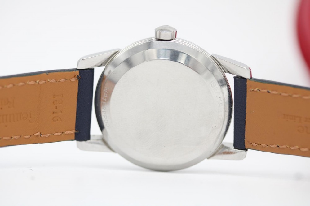 A vintage 1956 Omega Seamaster automatic wristwatch featuring a silver-coloured stainless steel case, off-white dial with gold-tone markers, and a navy blue leather strap. View X