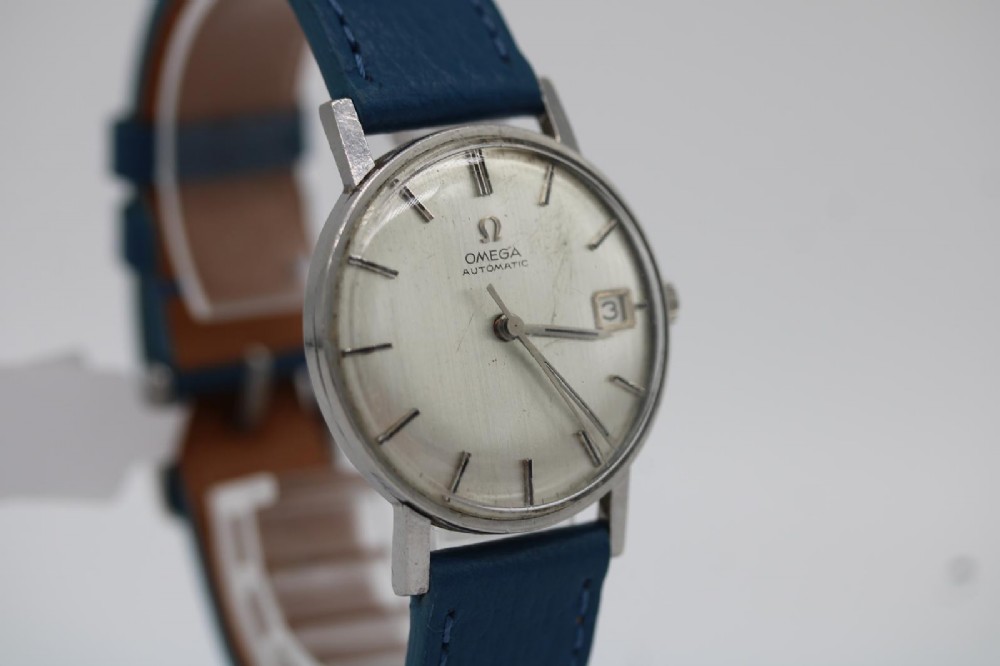 A 1963 stainless steel Omega Seamaster automatic wrist watch featuring a silver dial with baton indices, date window at three oclock, and a blue leather strap. View II