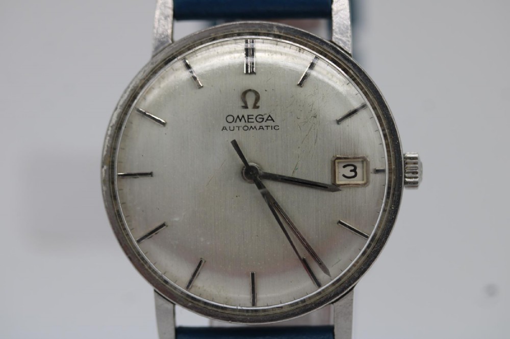 A 1963 stainless steel Omega Seamaster automatic wrist watch featuring a silver dial with baton indices, date window at three oclock, and a blue leather strap. View VII