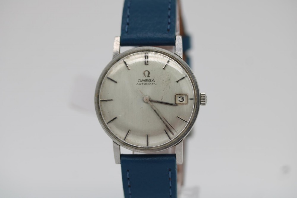 A 1963 stainless steel Omega Seamaster automatic wrist watch featuring a silver dial with baton indices, date window at three oclock, and a blue leather strap.