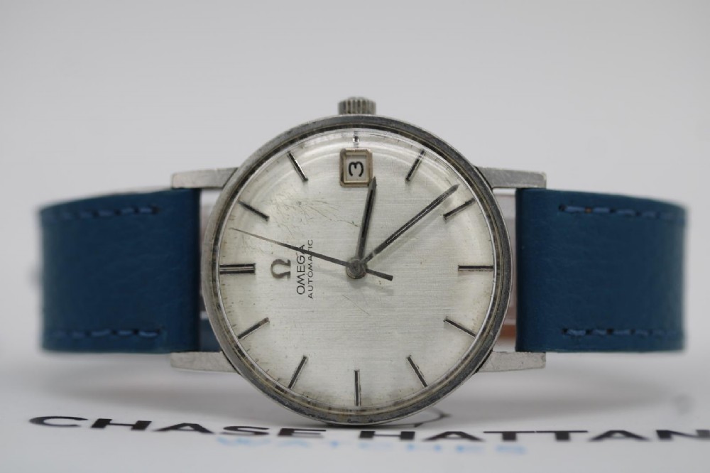 A 1963 stainless steel Omega Seamaster automatic wrist watch featuring a silver dial with baton indices, date window at three oclock, and a blue leather strap. View VIII
