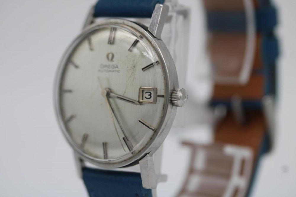 A 1963 stainless steel Omega Seamaster automatic wrist watch featuring a silver dial with baton indices, date window at three oclock, and a blue leather strap. View XIV