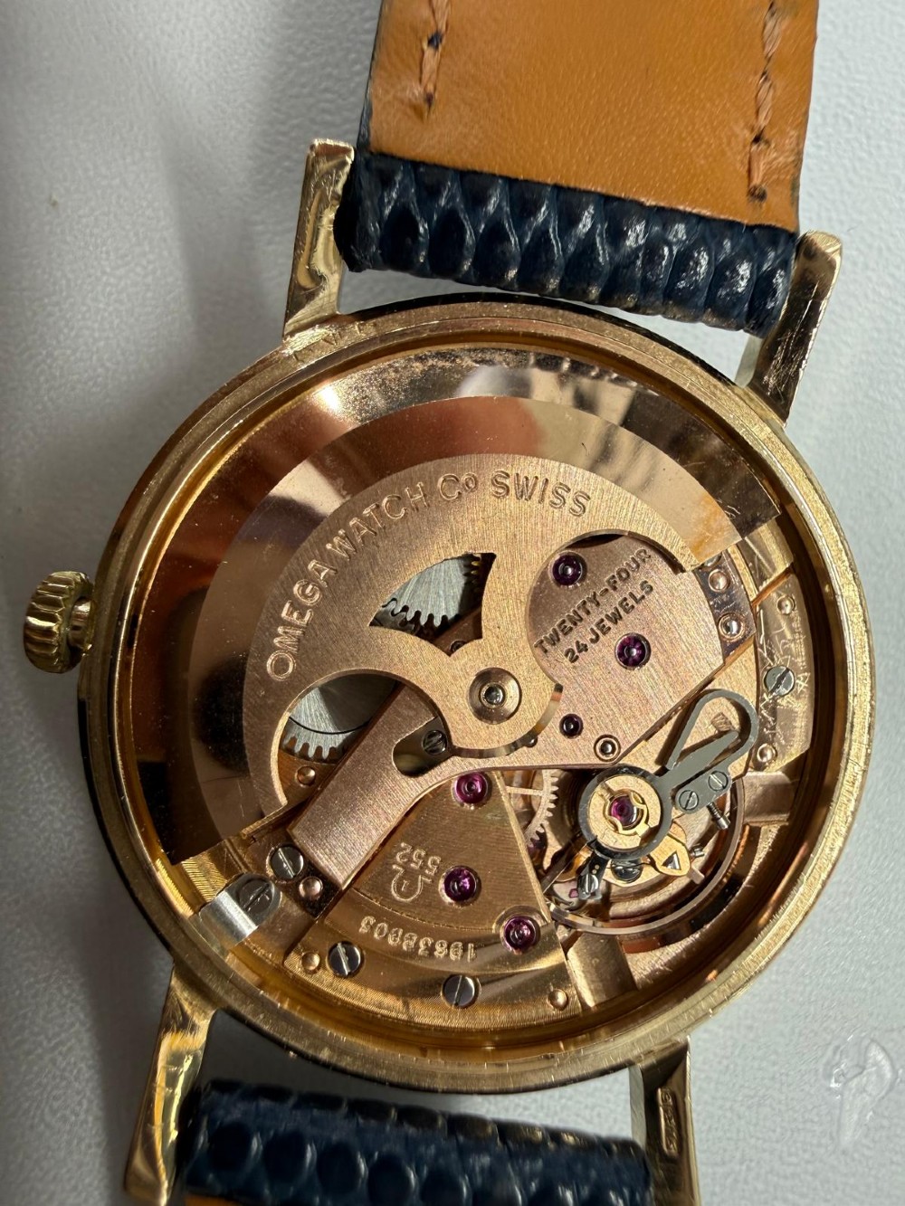 A 1962 Omega automatic wristwatch featuring a round 9ct gold case, silver dial with baton indices, and a blue textured leather strap. View III