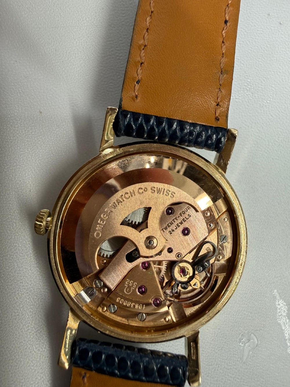 A 1962 Omega automatic wristwatch featuring a round 9ct gold case, silver dial with baton indices, and a blue textured leather strap. View V