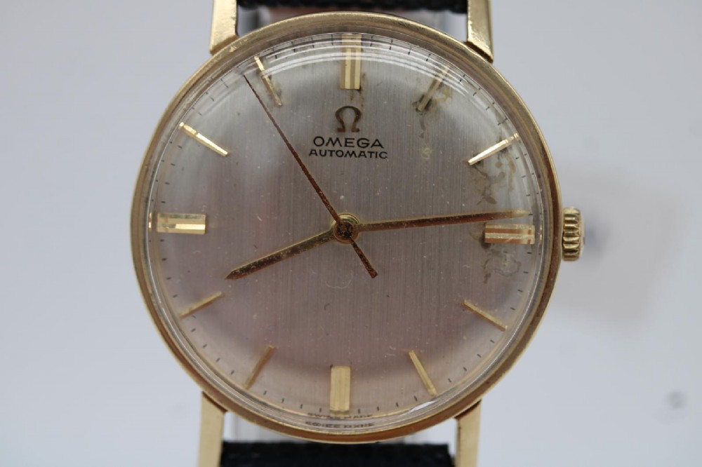 A 1962 Omega automatic wristwatch featuring a round 9ct gold case, silver dial with baton indices, and a blue textured leather strap. View VII