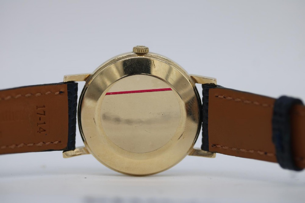 A 1962 Omega automatic wristwatch featuring a round 9ct gold case, silver dial with baton indices, and a blue textured leather strap. View XII