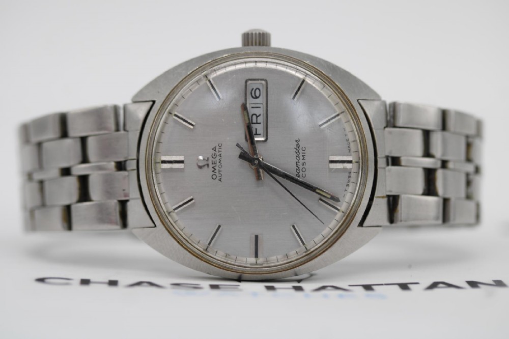 A vintage stainless steel Omega Seamaster Cosmic wristwatch featuring a silver dial with day-date window and metallic link bracelet. View VI