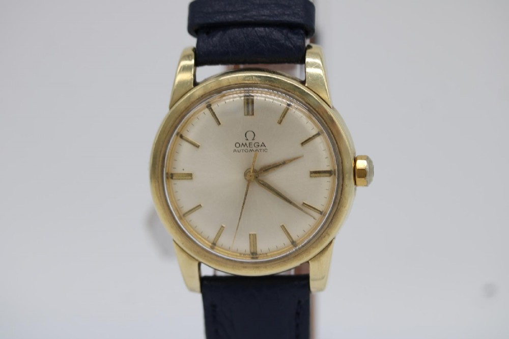 A gold-plated circular vintage wristwatch featuring a cream dial, gold hour indices, and a dark blue leather strap.