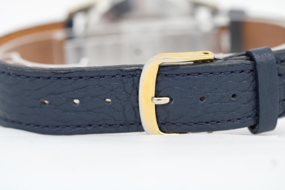 A gold-plated circular vintage wristwatch featuring a cream dial, gold hour indices, and a dark blue leather strap. View II