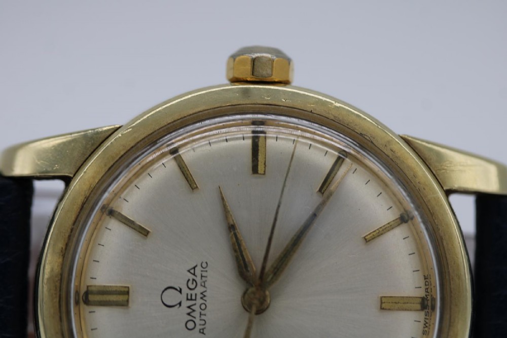 A gold-plated circular vintage wristwatch featuring a cream dial, gold hour indices, and a dark blue leather strap. View III