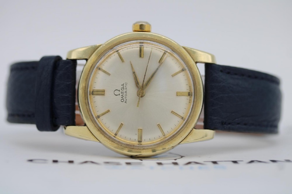A gold-plated circular vintage wristwatch featuring a cream dial, gold hour indices, and a dark blue leather strap. View IV