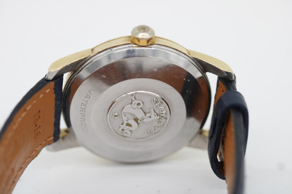 A gold-plated circular vintage wristwatch featuring a cream dial, gold hour indices, and a dark blue leather strap. View V