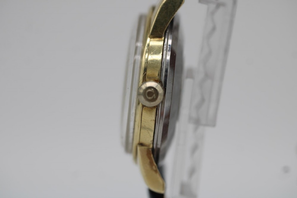 A gold-plated circular vintage wristwatch featuring a cream dial, gold hour indices, and a dark blue leather strap. View VI