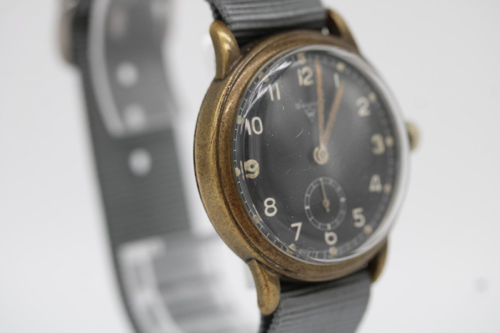 A close-up photograph of a 1940s Wagner German military wristwatch featuring a black dial, luminous Arabic numerals, a small sub-seconds dial, and a patinated brass case. View II