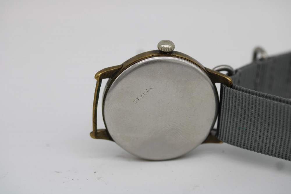 A close-up photograph of a 1940s Wagner German military wristwatch featuring a black dial, luminous Arabic numerals, a small sub-seconds dial, and a patinated brass case. View XII
