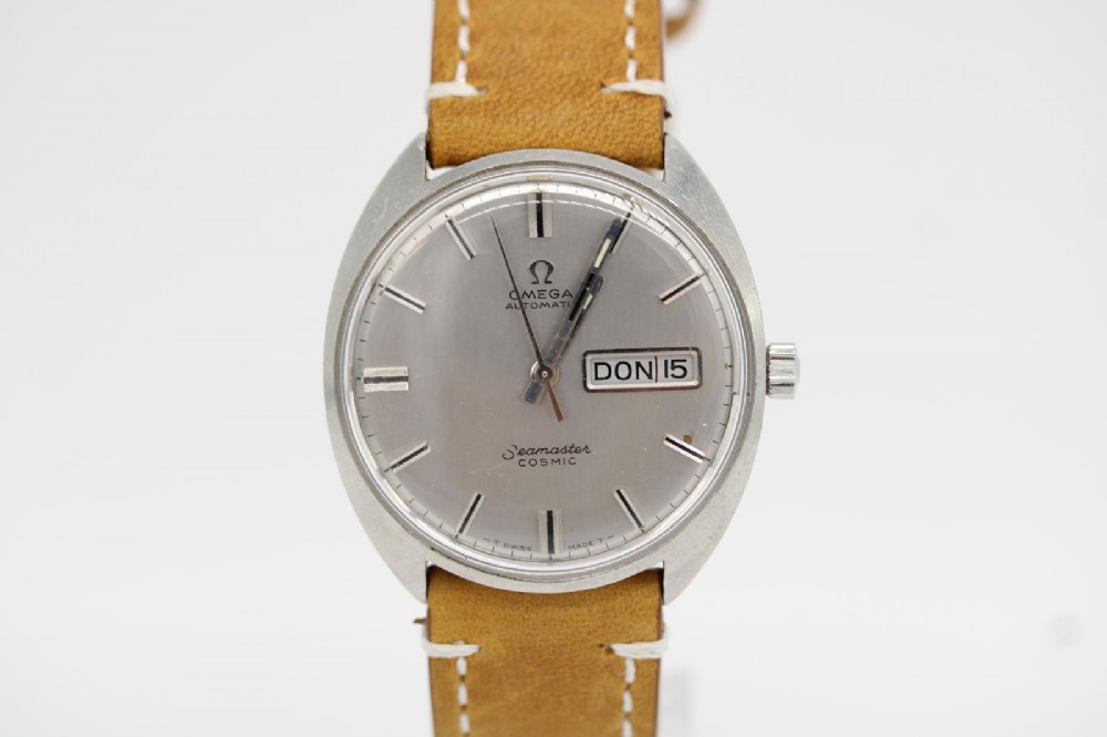 A vintage stainless steel Omega Seamaster Cosmic automatic wristwatch featuring a silver dial with day-date aperture and a tan leather strap with white stitching.