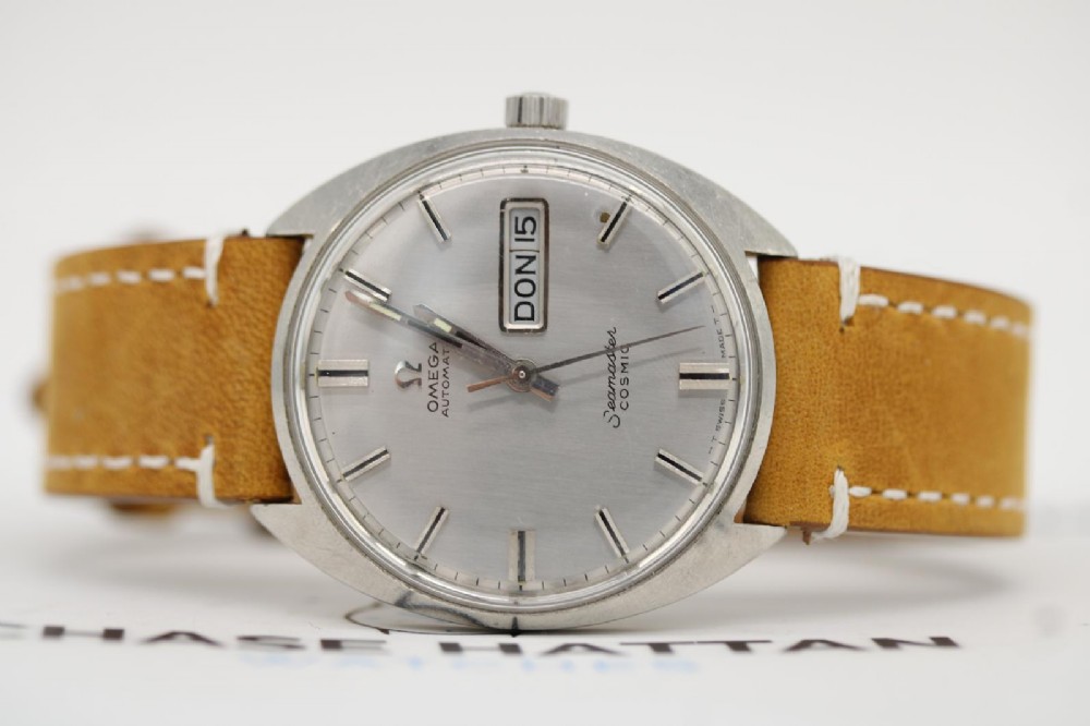 A vintage stainless steel Omega Seamaster Cosmic automatic wristwatch featuring a silver dial with day-date aperture and a tan leather strap with white stitching. View III