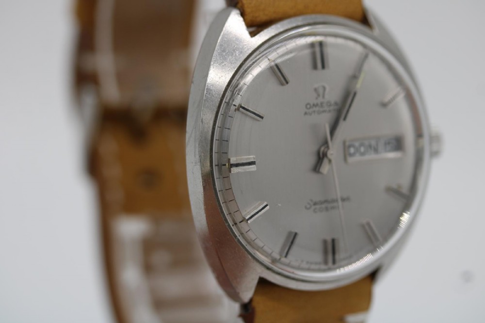 A vintage stainless steel Omega Seamaster Cosmic automatic wristwatch featuring a silver dial with day-date aperture and a tan leather strap with white stitching. View VI