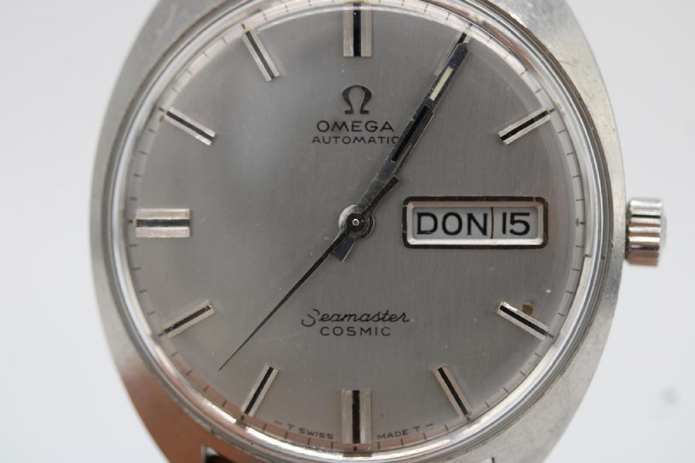 A vintage stainless steel Omega Seamaster Cosmic automatic wristwatch featuring a silver dial with day-date aperture and a tan leather strap with white stitching. View VII