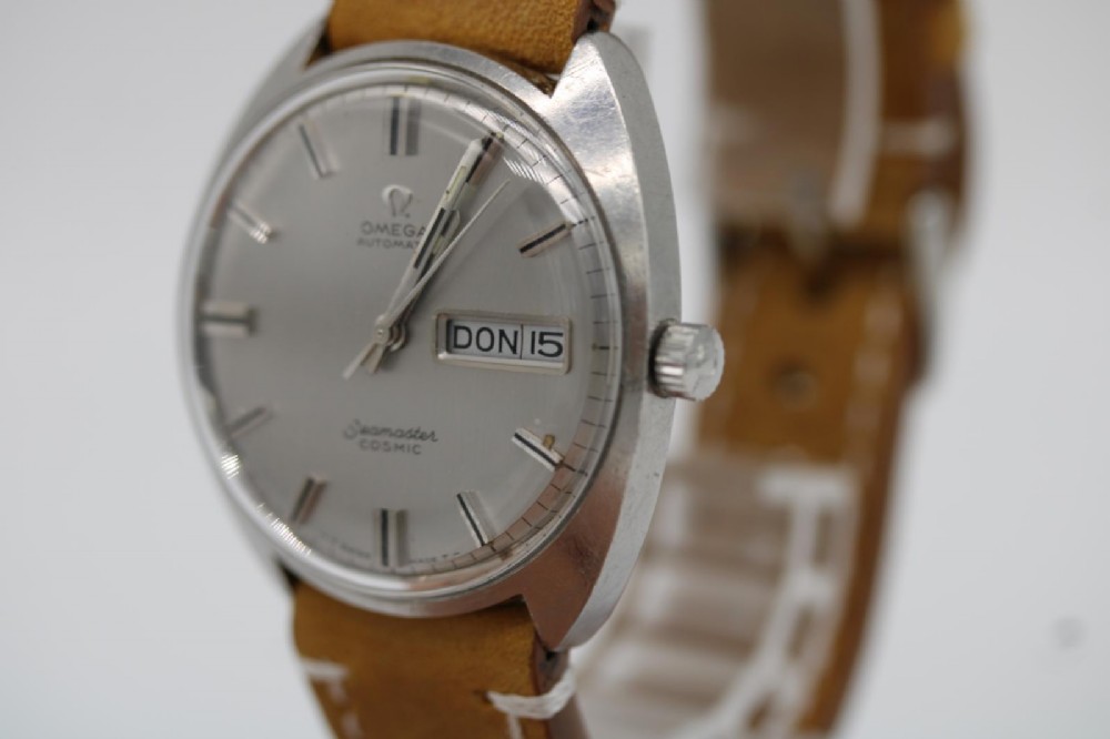 A vintage stainless steel Omega Seamaster Cosmic automatic wristwatch featuring a silver dial with day-date aperture and a tan leather strap with white stitching. View IX