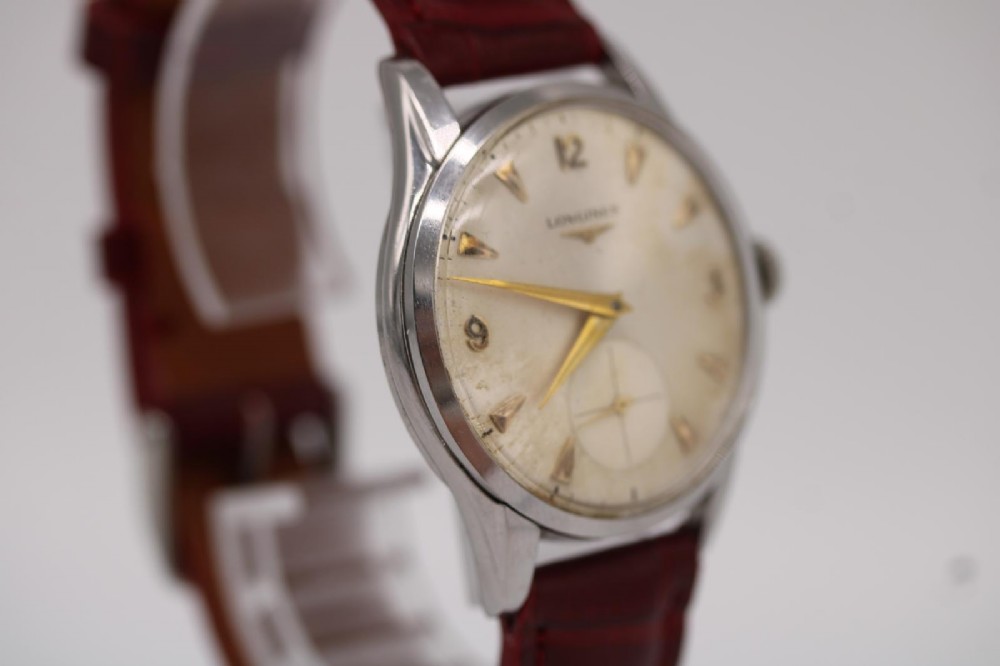 A 1950s Longines wristwatch with a stainless steel case, off-white dial with gold-tone hour markers, sub-seconds dial, and a burgundy leather strap. View IV