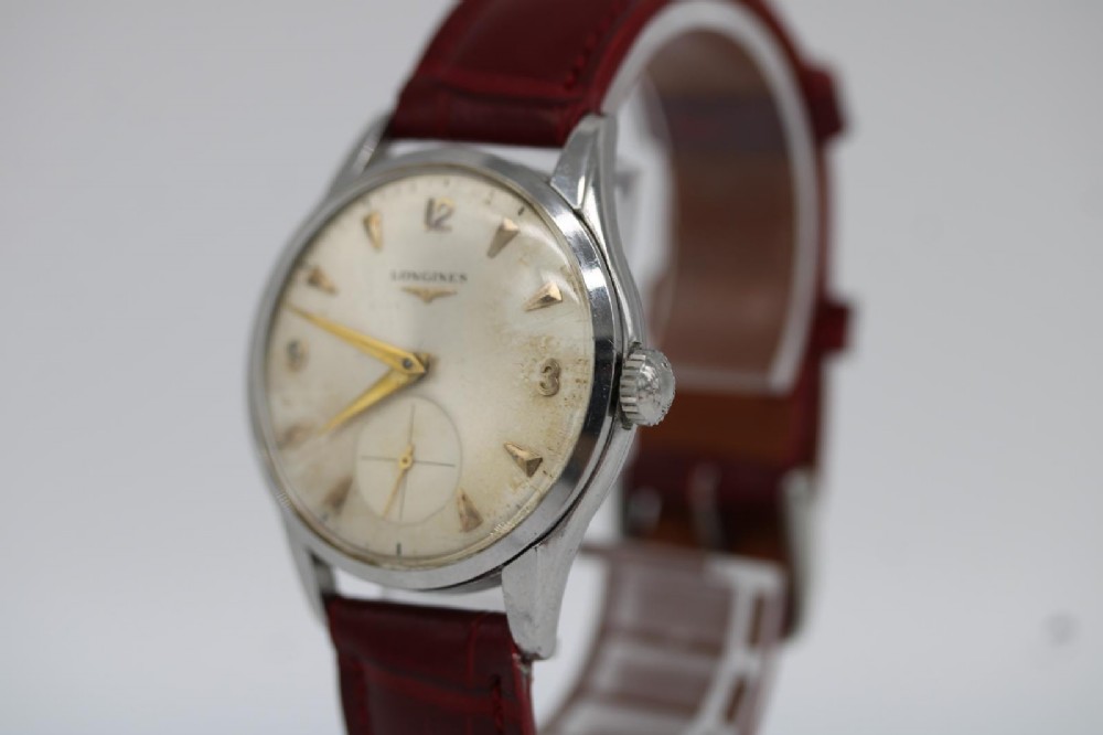 A 1950s Longines wristwatch with a stainless steel case, off-white dial with gold-tone hour markers, sub-seconds dial, and a burgundy leather strap. View V