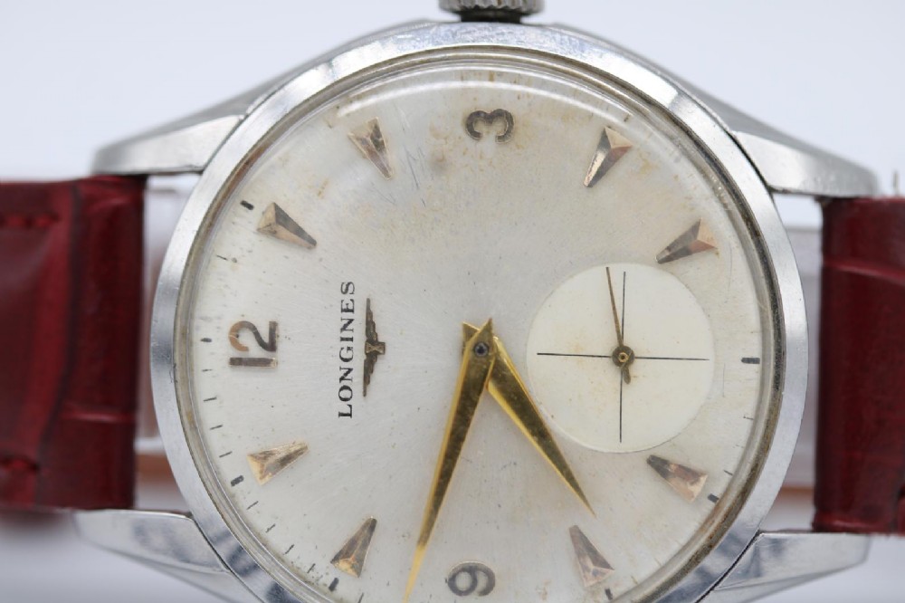 A 1950s Longines wristwatch with a stainless steel case, off-white dial with gold-tone hour markers, sub-seconds dial, and a burgundy leather strap. View VI