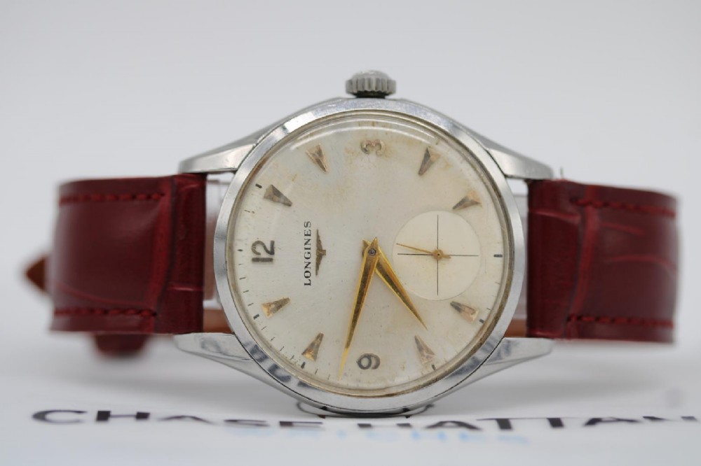 A 1950s Longines wristwatch with a stainless steel case, off-white dial with gold-tone hour markers, sub-seconds dial, and a burgundy leather strap. View VII