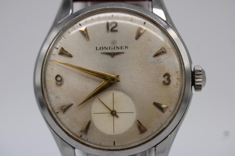 A 1950s Longines wristwatch with a stainless steel case, off-white dial with gold-tone hour markers, sub-seconds dial, and a burgundy leather strap. View IX