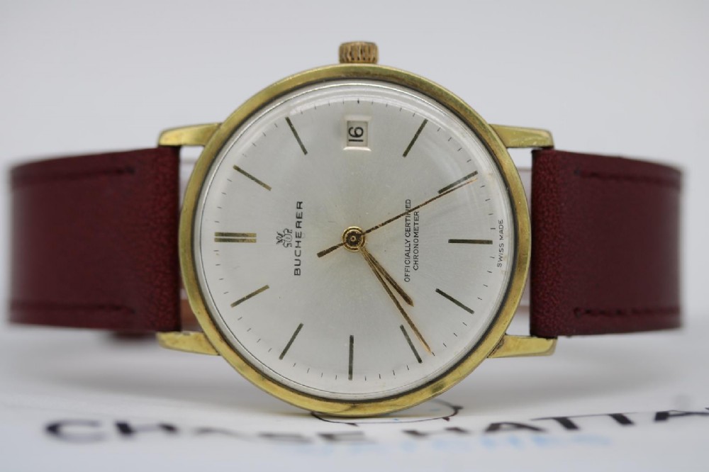 A circular vintage Bucherer gold-plated automatic wristwatch featuring a silver dial, gold hour indices, a date aperture at three oclock, and a burgundy leather strap. View IV