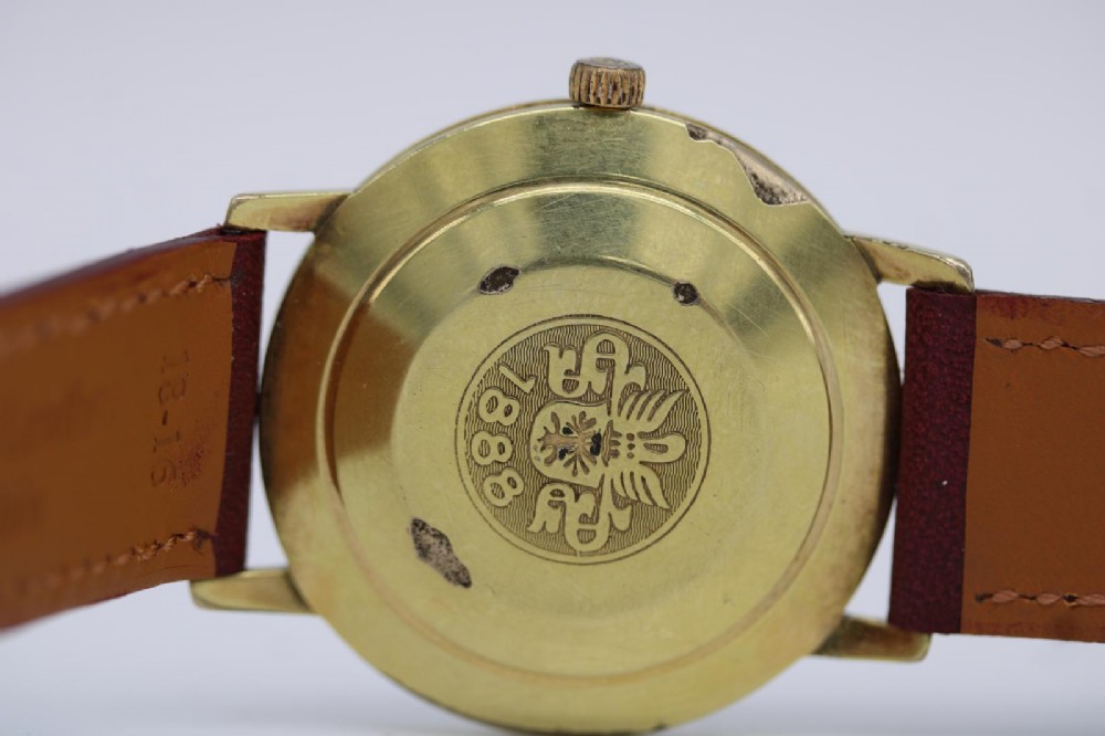 A circular vintage Bucherer gold-plated automatic wristwatch featuring a silver dial, gold hour indices, a date aperture at three oclock, and a burgundy leather strap. View VI