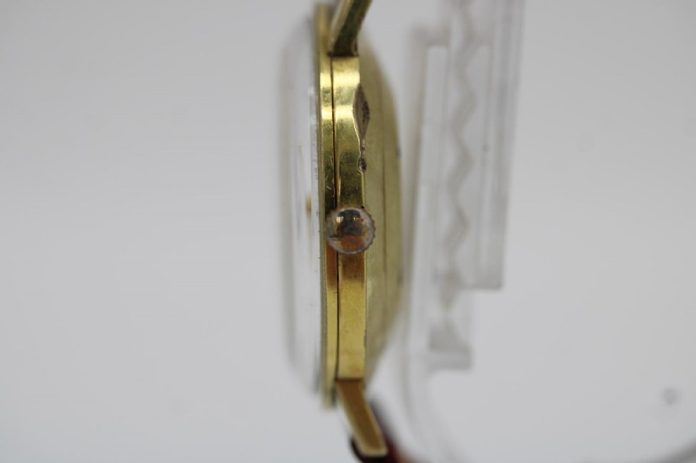 A circular vintage Bucherer gold-plated automatic wristwatch featuring a silver dial, gold hour indices, a date aperture at three oclock, and a burgundy leather strap. View VII