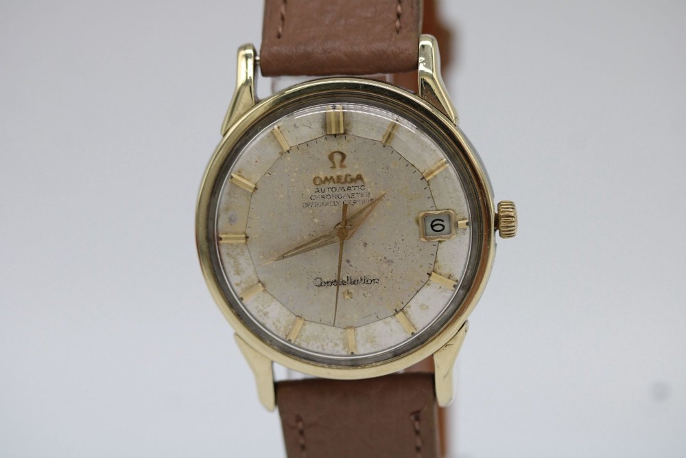 A vintage gold-plated Omega Constellation wristwatch featuring a faceted pie-pan dial, date window, and a brown leather strap.
