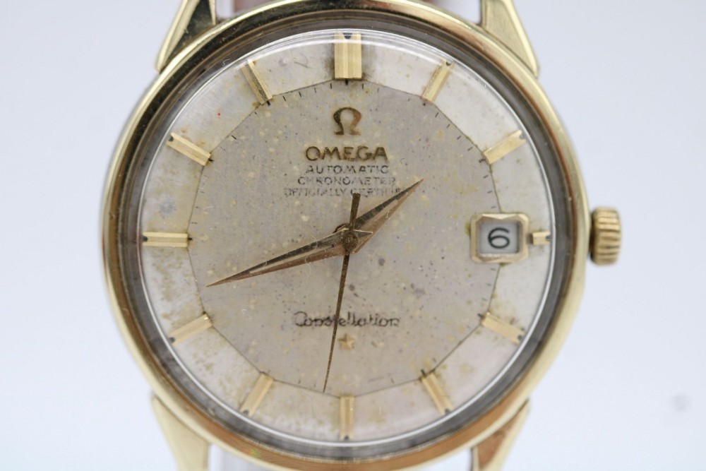 A vintage gold-plated Omega Constellation wristwatch featuring a faceted pie-pan dial, date window, and a brown leather strap. View II