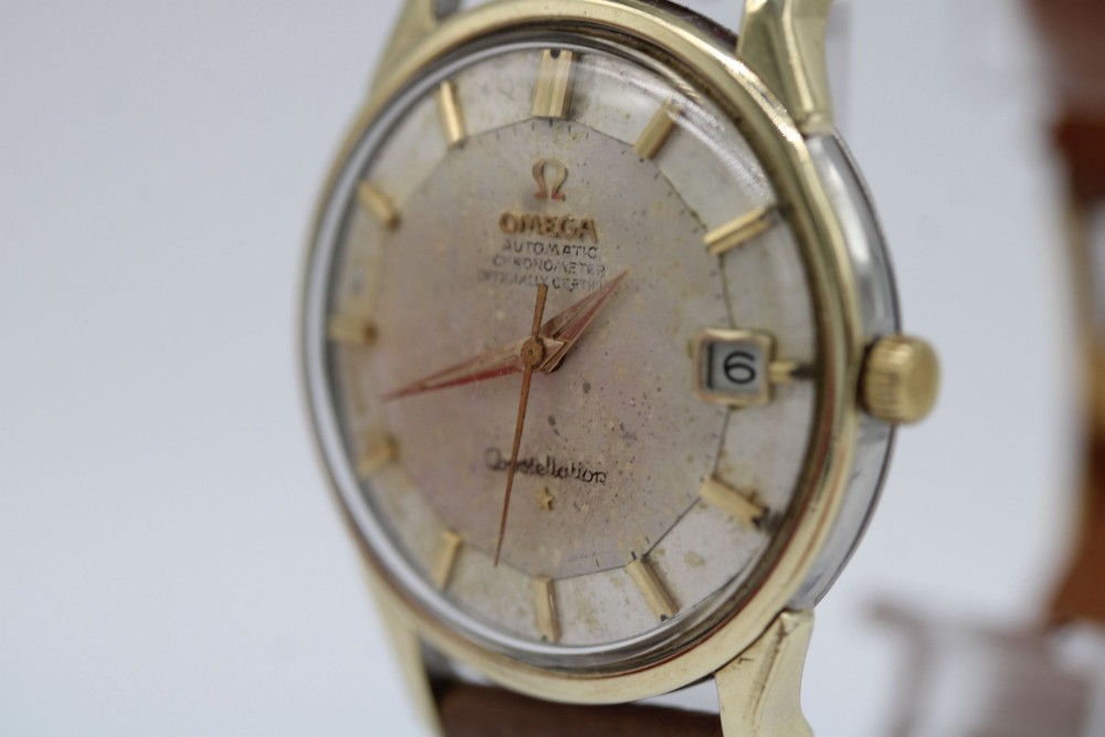 A vintage gold-plated Omega Constellation wristwatch featuring a faceted pie-pan dial, date window, and a brown leather strap. View III