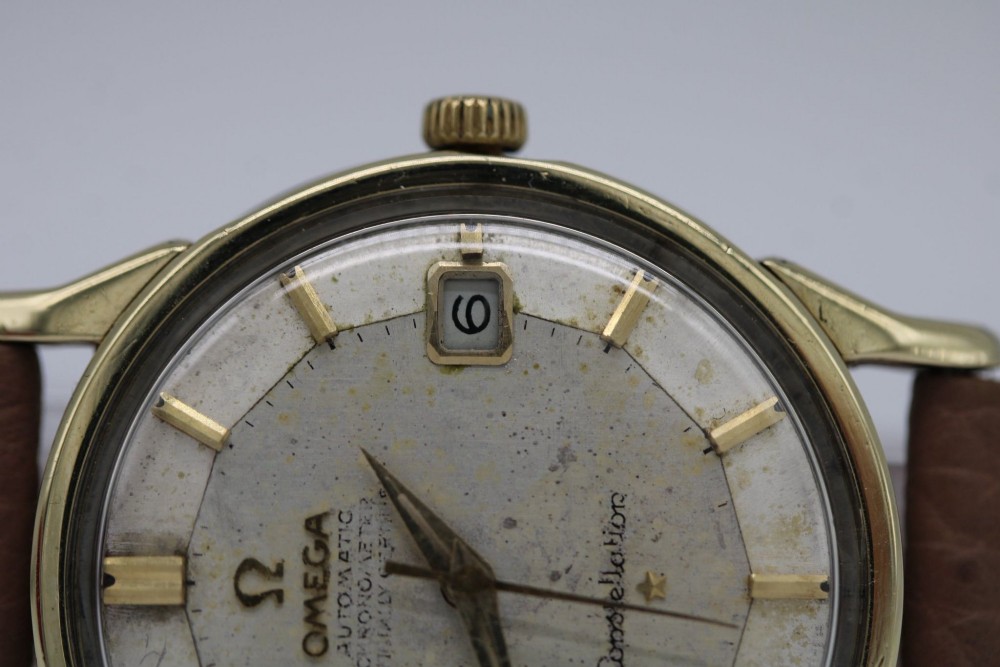 A vintage gold-plated Omega Constellation wristwatch featuring a faceted pie-pan dial, date window, and a brown leather strap. View XI