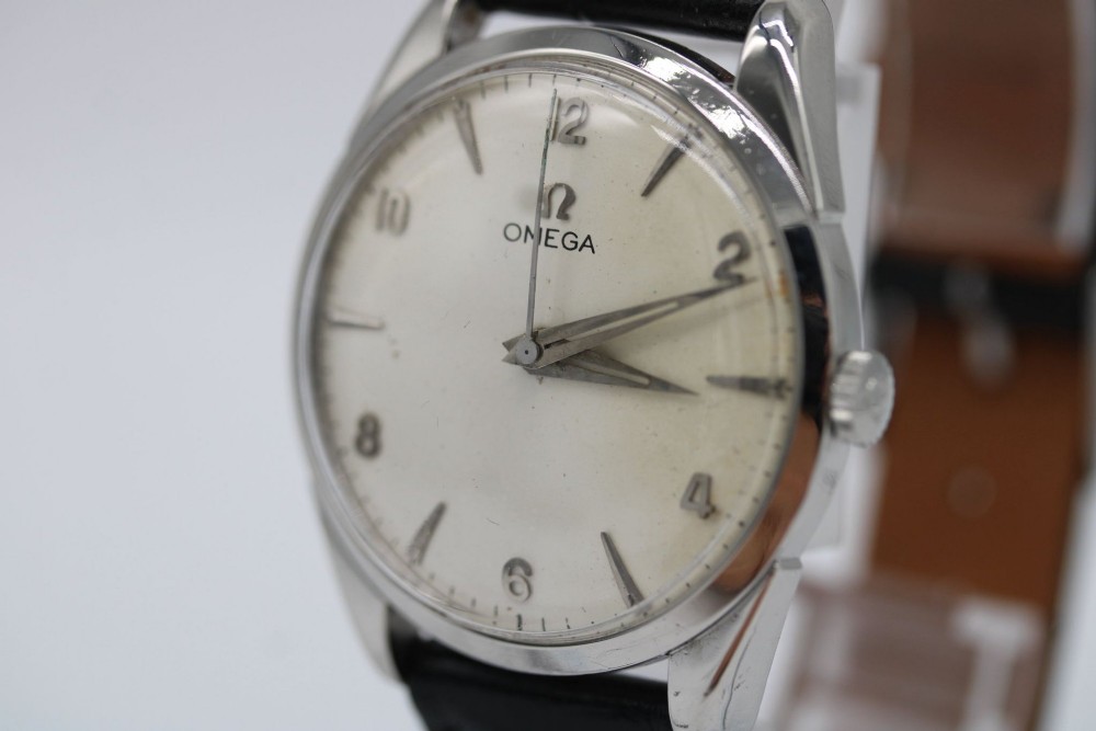 A 1960s Omega stainless steel manual-wind wristwatch featuring a silver dial with silver-toned Arabic numerals and indices on a black leather strap. View VI
